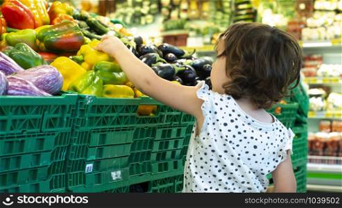 Child shopping peppers in supermarket. Concept for buying fruits and vegetables in hypermarket. Little girl hold shopping basket.