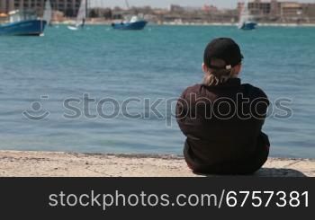 child sitting at the seashore watching the sailing yachts