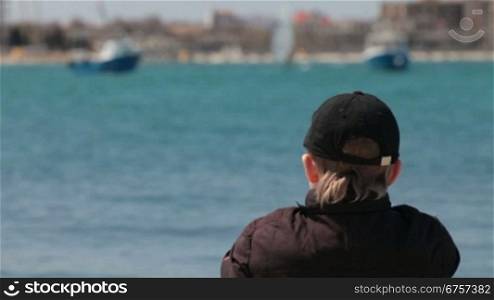 child sitting at the seashore watching the sailing yachts