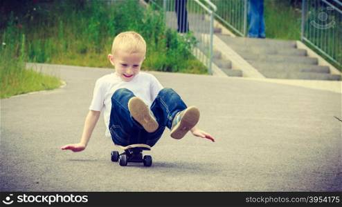 Child sitting on skateboard outdoor. Active boy skateboarding on pavement sidewalk. Kid practicing outside. . Child kid sitting on skateboard having fun outdoor