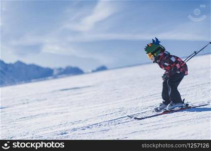 Child skiing in mountains. Active teenage kid with safety helmet, goggles and ski poles running down ski slope. Snowy landscape, sunny day in winter season. Child Skiing in the Mountains