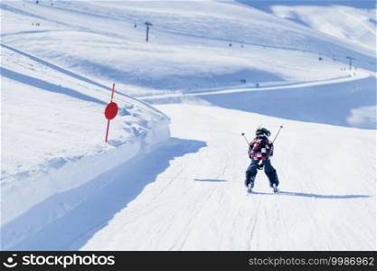 Child skiing in mountains. Active teenage kid with safety helmet, goggles and ski poles running down ski slope.  Snowy landscape, sunny day in winter season. Child Skiing in the Mountains 