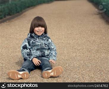 Child smiles and sits on the ground in park