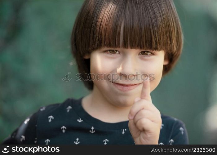 Child smiles and wags a finger, face portrait on blurry background