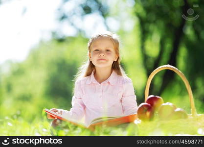 Child with book having picnic in summer park. Girl in park