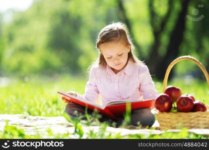 Child with book having picnic in summer park. Girl in park