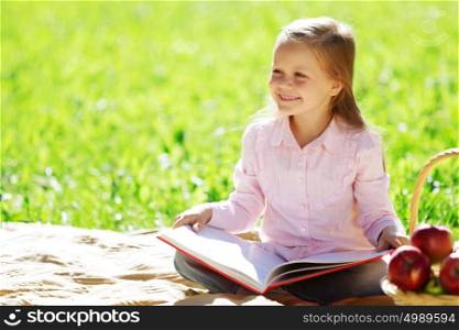 Child with book having picnic in summer park. Girl in park