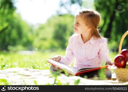 Child with book having picnic in summer park. Girl in park