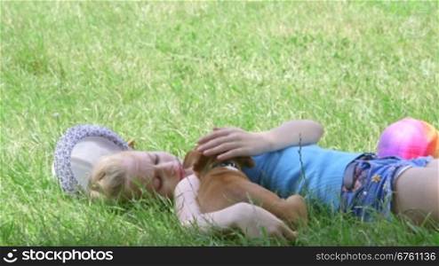 Child with puppy dog resting in shade of tree on grass in summer day