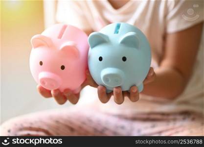 Child woman hand hold blue and pink piggy bank for saving money for education study or investment , Save money concept, daughter hands holding pink piggy bank