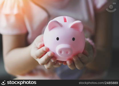 Child woman hand hold pink piggy bank for saving money for education study or investment , Save money concept, daughter hands holding pink piggy bank