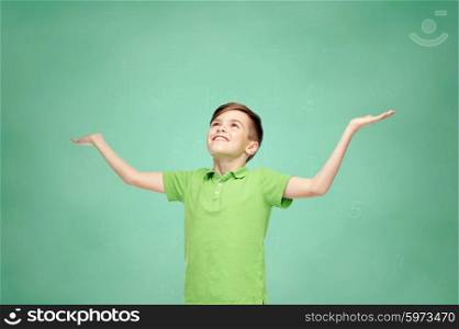 childhood, achievement, gladness and people concept - happy smiling boy in green polo t-shirt raising hands and looking up over green school chalk board background