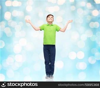 childhood, achievement, gladness and people concept - happy smiling boy in green polo t-shirt raising hands and looking up over blue holidays lights background