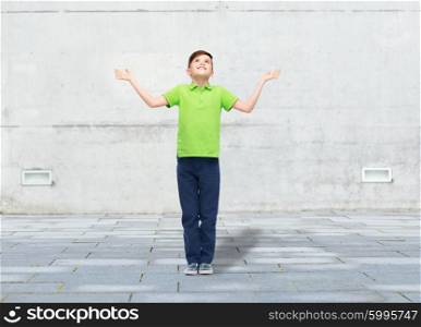 childhood, achievement, gladness and people concept - happy smiling boy in green polo t-shirt raising hands and looking up over urban street background