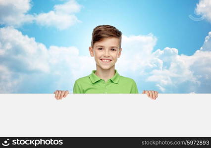 childhood, advertisement and people concept - happy smiling boy in green polo t-shirt holding white blank board over blue sky and clouds background