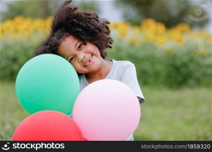 childhood and back emotion concept- little african american curly hair girl playing bolloons near sunflower field at outdoor.