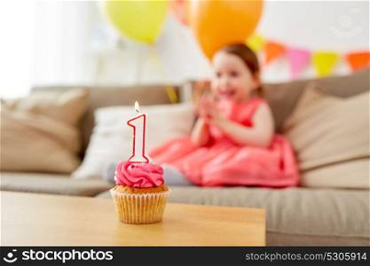 childhood and celebration concept - birthday cupcake with candle for one year old baby girl anniversary at home party. birthday cupcake for child one year anniversary