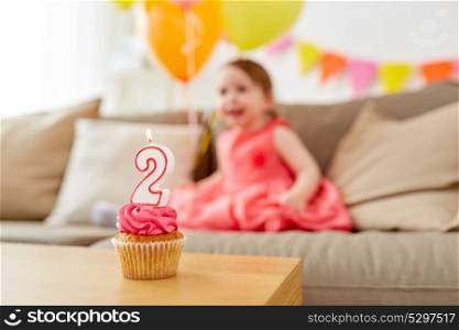 childhood and celebration concept - birthday cupcake with candle for two year old baby girl at home party. birthday cupcake for two year old baby girl