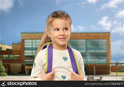 childhood and education concept - happy little girl with backpack over school on background. happy little girl with school backpack