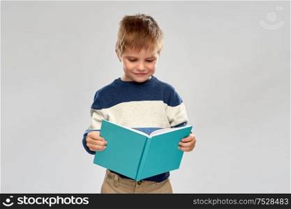 childhood and education concept - smiling little boy reading book over grey background. smiling little boy reading book