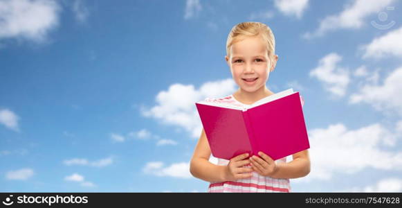 childhood and education concept - smiling little girl reading book over blue sky and clouds background. smiling little girl reading book