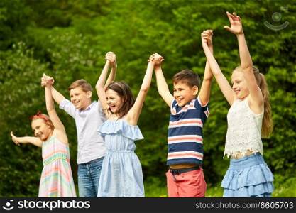 childhood and friendship concept - happy kids holding raised hands in summer park. happy kids holding raised hands in summer park