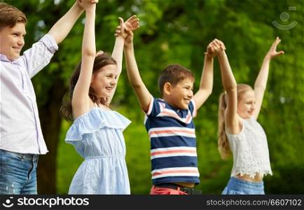 childhood and friendship concept - happy kids holding raised hands in summer park. happy kids holding raised hands in summer park