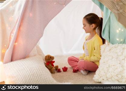 childhood and hygge concept - happy little girl playing tea party with teddy bear in kids tent at home. little girl playing tea party in kids tent at home. little girl playing tea party in kids tent at home