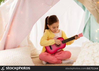 childhood and hygge concept - happy little girl playing toy guitar in kids tent at home. girl playing toy guitar in kids tent at home. girl playing toy guitar in kids tent at home