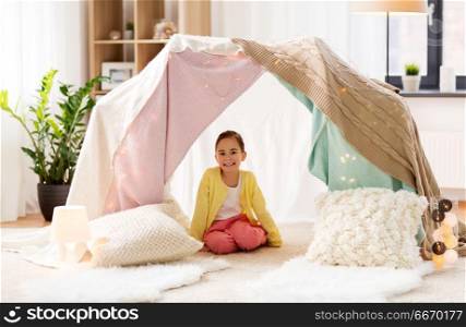 childhood and hygge concept - happy little girl sitting in kids tent at home. little girl sitting in kids tent at home. little girl sitting in kids tent at home