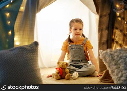 childhood and hygge concept - happy little girl with toys in kids tent at home. little girl with toys in kids tent at home