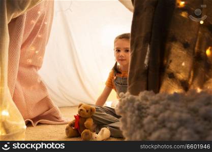 childhood and hygge concept - happy little girl with toys in kids tent at home. little girl with toys in kids tent at home