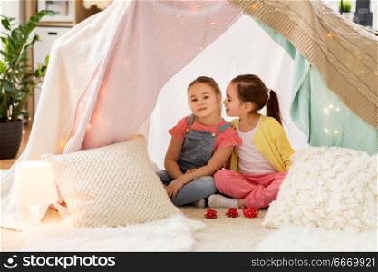 childhood and hygge concept - happy little girls playing tea party with toy crockery in kids tent at home and sharing secrets. little girl playing tea party in kids tent at home. little girl playing tea party in kids tent at home