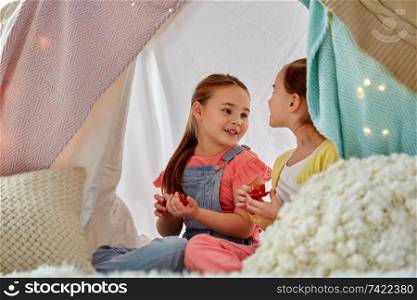 childhood and hygge concept - happy little girls playing tea party with toy crockery in kids tent at home. little girl playing tea party in kids tent at home