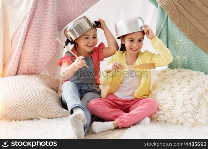 childhood and hygge concept - happy little girls with cooking pots playing in kids tent at home. girls with kitchenware playing in tent at home. girls with kitchenware playing in tent at home