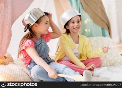 childhood and hygge concept - happy little girls with cooking pots playing in kids tent at home. girls with kitchenware playing in tent at home