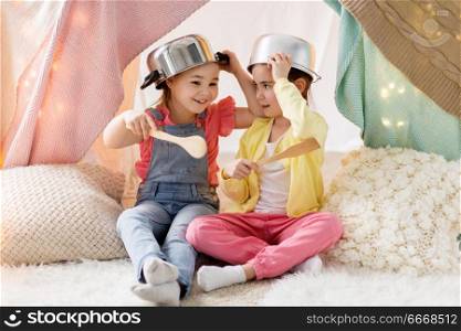 childhood and hygge concept - happy little girls with cooking pots playing in kids tent at home. girls with kitchenware playing in tent at home. girls with kitchenware playing in tent at home