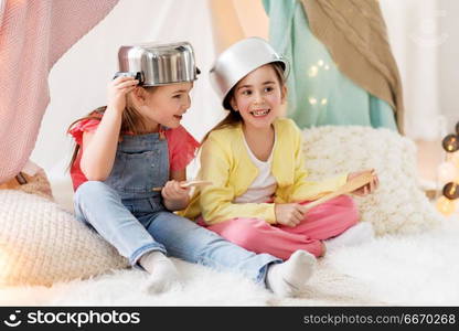 childhood and hygge concept - happy little girls with cooking pots playing in kids tent at home. girls with kitchenware playing in tent at home. girls with kitchenware playing in tent at home