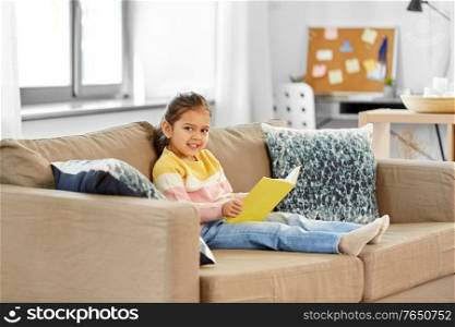 childhood and leisure concept - happy smiling little girl reading book at home. happy smiling little girl reading book at home