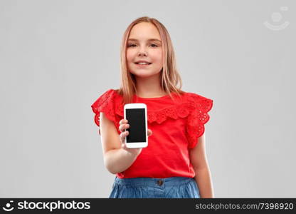 childhood and people concept - beautiful smiling girl in red shirt and skirt showing smartphone over grey background. beautiful smiling girl showing smartphone