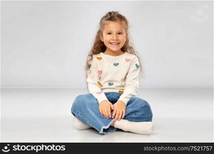 childhood and people concept - beautiful smiling girl sitting on floor over grey background. beautiful smiling girl sitting on floor