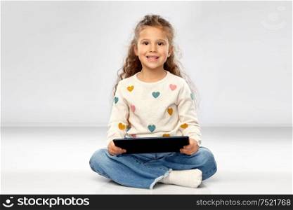 childhood and people concept - beautiful smiling girl with tablet computer sitting on floor over grey background. smiling girl with tablet computer sitting on floor