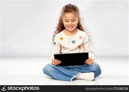 childhood and people concept - beautiful smiling girl with tablet computer sitting on floor over grey background. smiling girl with tablet computer sitting on floor