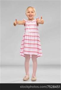 childhood and people concept - beautiful smiling little girl in striped dress showing thumbs up over grey background. beautiful little smiling girl showing thumbs up