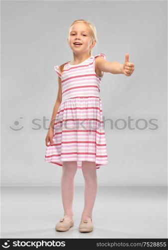 childhood and people concept - beautiful smiling little girl in striped dress showing thumbs up over grey background. beautiful smiling little girl showing thumbs up