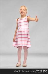childhood and people concept - beautiful smiling little girl in striped dress showing thumbs up over grey background. beautiful smiling little girl showing thumbs up