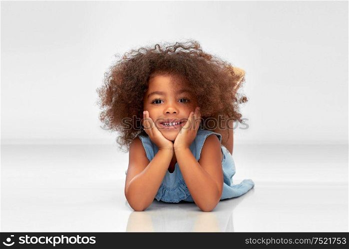 childhood and people concept - happy little african american girl lying on floor over grey background. happy little african american girl lying on floor