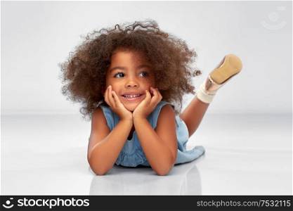 childhood and people concept - happy little african american girl lying on floor over grey background. happy little african american girl lying on floor