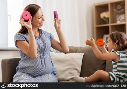 childhood and people concept - happy pregnant mother and little daughter playing with toy blocks at home. pregnant mother and daughter with toy blocks