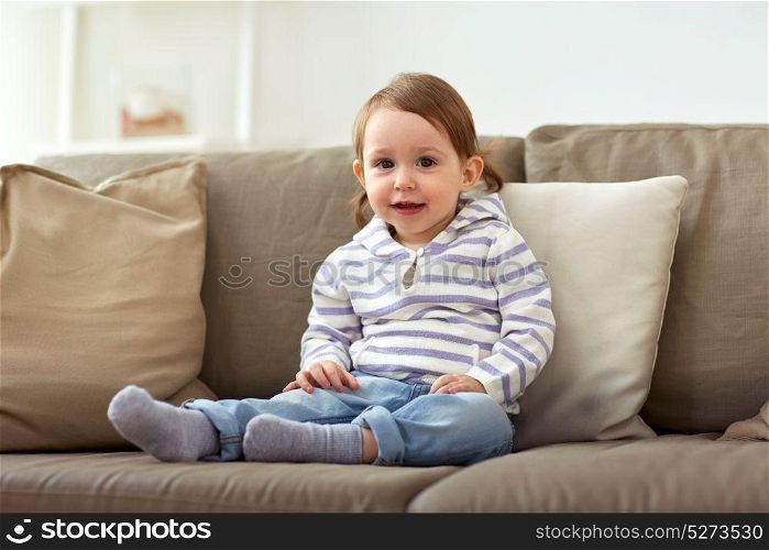 childhood and people concept - happy smiling baby girl sitting on sofa at home. happy smiling baby girl sitting on sofa at home